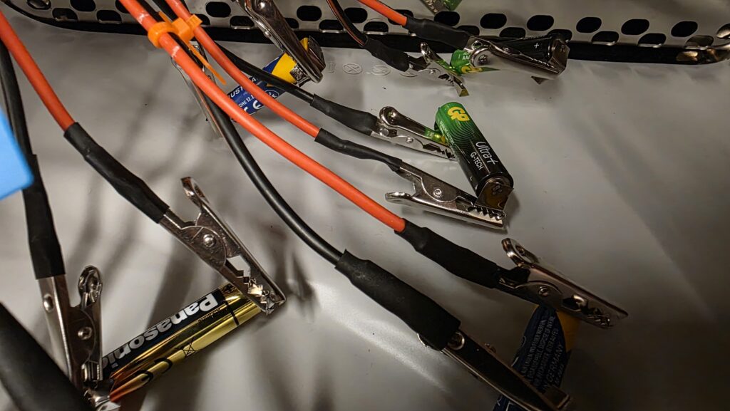 Different brands of AAA batteries connected for profiling inside the temperature chamber.